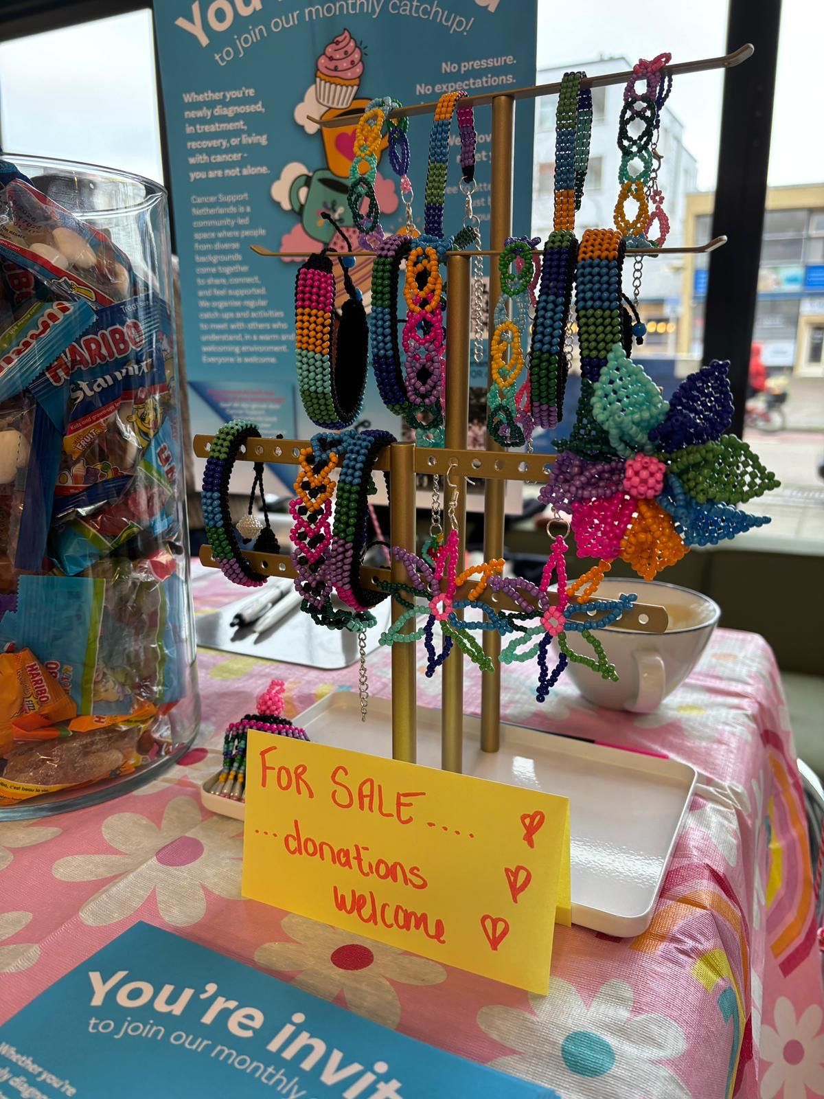 Colourful handmade beaded bracelets on a stand at a CSN table, with a sign saying For sale, donations welcome