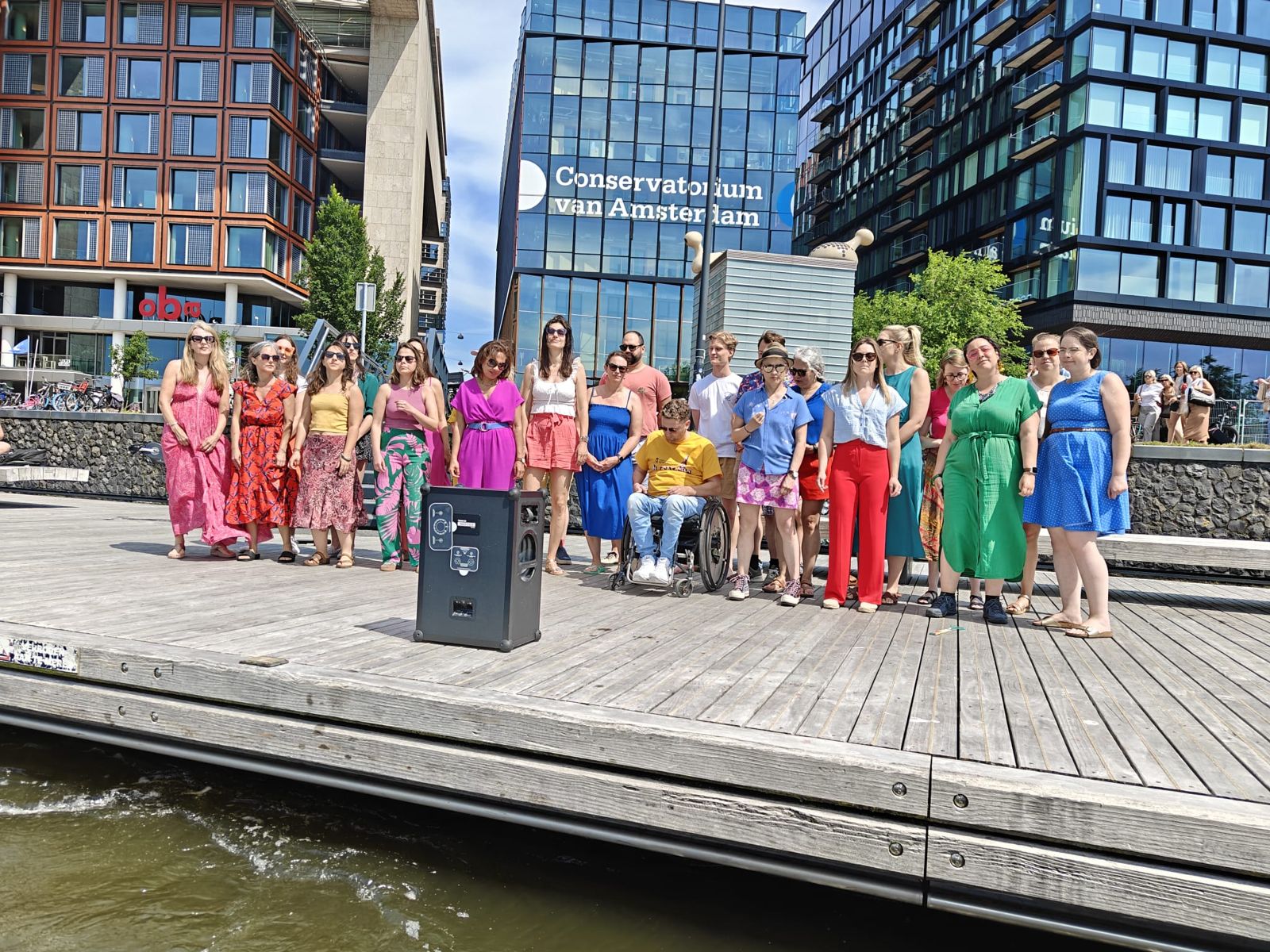 Members in bright summer clothes standing together on a wooden quay by the water in Amsterdam