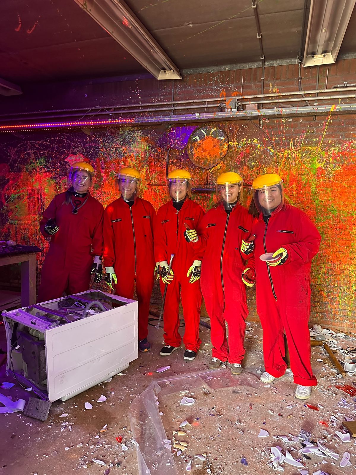 Five members in red overalls, gloves and face shields smiling in a smash room after a session