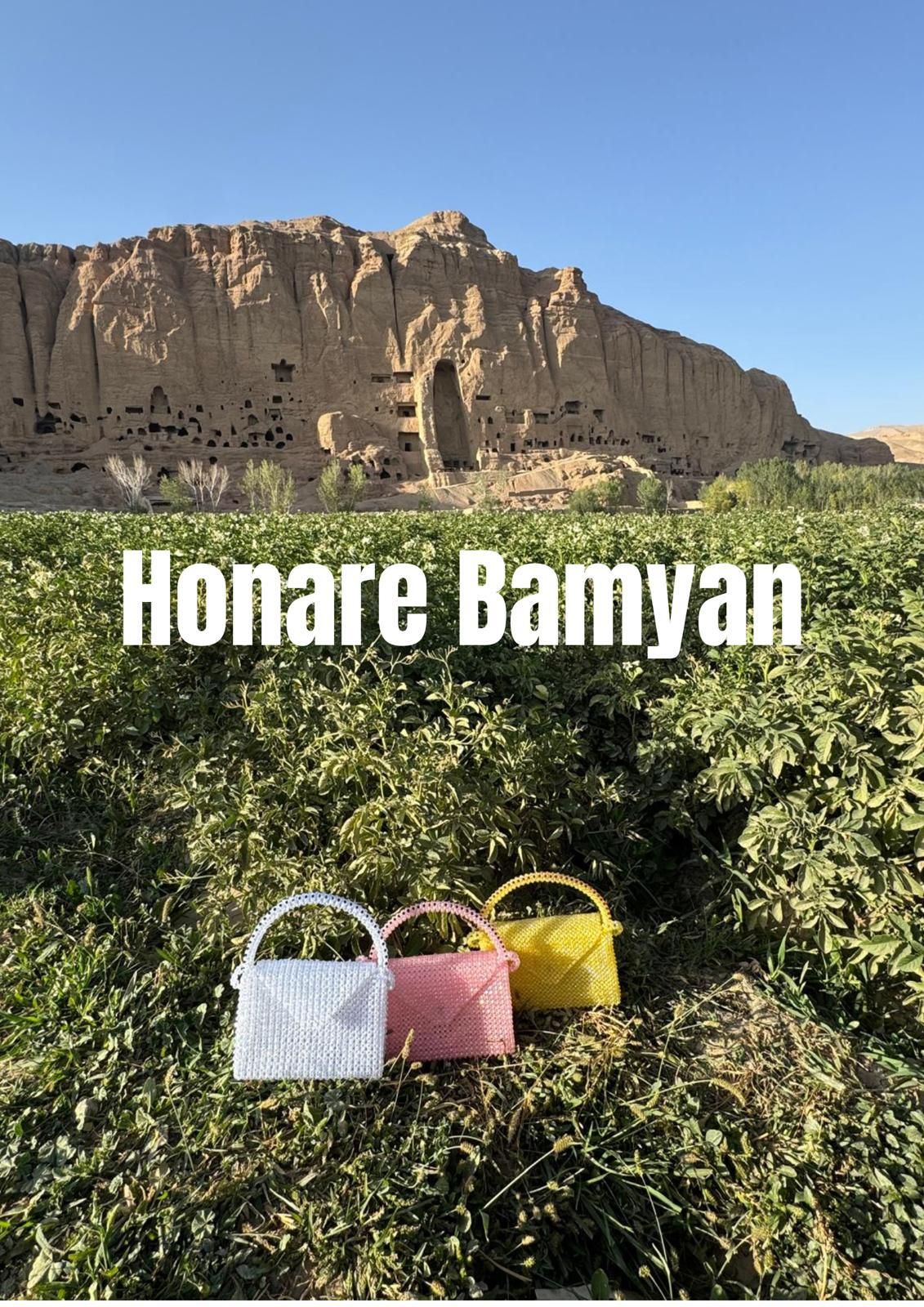 Three beaded handbags, white, pink and yellow, in a green field in front of the cliffs of Bamyan